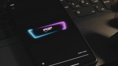 Cep telefonu ekranında dinamik neon çerçeveli popüler kültür yazıları. Dalgalar etki ediyor. Erkek el parmaklarıyla neşeyle çırpınıyor. Eğlence konsepti.