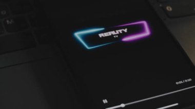 Cep telefonu ekranında dinamik mavi neon çerçeveli realite TV yazıları. Dalgalar etki ediyor. Erkek el parmaklarıyla neşeyle çırpınıyor. Eğlence konsepti.