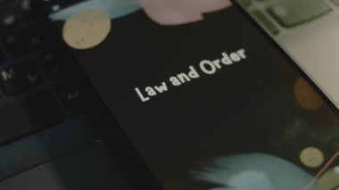 Akıllı telefon ekranında Law and Order yazıları var. Bokeh ışıklarıyla siyah arkaplan üzerine grafiksel sunum. Işık ışınları. Hukuki kavram.