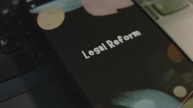 Akıllı telefon ekranında yasal reform yazıları var. Bokeh ışıklarıyla siyah arkaplan üzerine grafiksel sunum. Işık ışınları. Hukuki kavram.