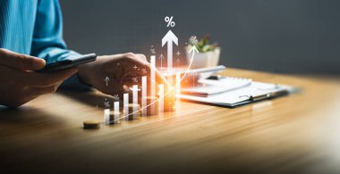 İstiflenmiş Paralar ve Yükselen Çubuk Grafik Çizgileri, Artan Kârlar, Ekonomik Eğilimler ve Stratejik Yatırım Fırsatları ile Akıllı Telefon Kullanarak Finansal Büyümeyi Analiz Eden İşadamı