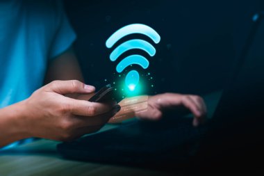 Elleri Cep Telefonu ve Laptop ile Parlayan Wifi Simgesi ve Teknoloji Konseptinde Giriş Ekranı Kullanıyor. Çevrimiçi İletişim ve Veri Takası için Dijital Kablosuz İnternet Bağlantısı ve Güvenli Erişim