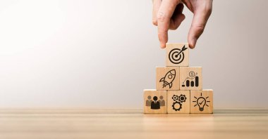 Girişim büyümesini, takım çalışmasını, finansal başarıyı, hedef başarısını, başarılı ve yenilikçi bir iş stratejisi oluşturma adımlarını simgeleyen iş simgeleriyle ahşap blokların elle düzenlenmesi