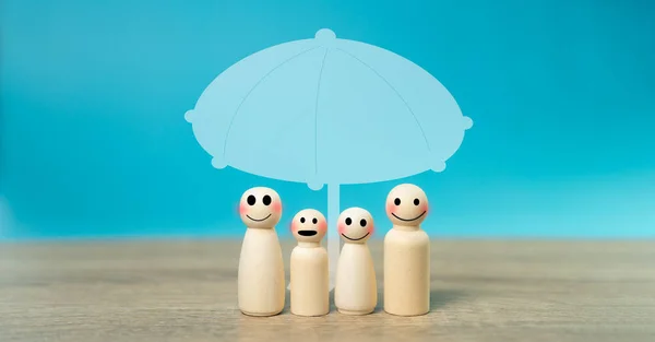 Concept of insurance, protection, safety, family security, wooden family dolls, and an open umbrella. ,on a bright blue background, with copy space.