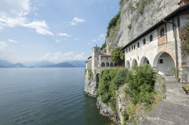Ünlü Eremo di Santa Caterina del Sasso 'nun manzarası, İtalya' daki taş inzivasının Saint Catherine 'i. Maggiore Gölü 'nün mavi suları solda. Arka planda İtalyan Alpleri ve mavi gökyüzü
