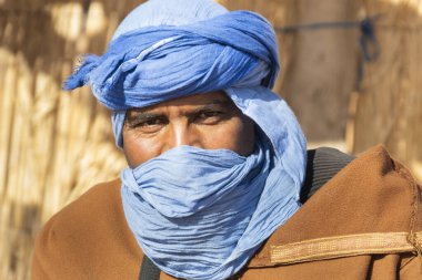 Sahra Çölü 'ndeki Tuareg Rehberi güneşli bir günde turistlere anlatıyor ve anlatıyor. Seçici odak, bulanık kayalık dağ ve mavi gökyüzü. Cezayir