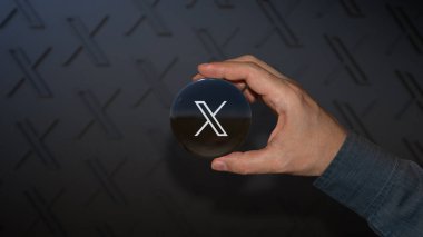X logosu olan yuvarlak bir rozet tutan bir erkek el sosyal ağın yeni adı Twitter..