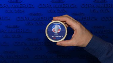 Bir erkek el üzerinde CONMEBOL COPA AMERICA 2024 Futbol Şampiyonası logosu bulunan yuvarlak bir plakete sahiptir..