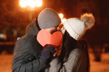 Sevgililer Günü gebeliği. Genç bir çiftin açık hava gece portresi. Avrupa 'nın caddesinde poz vermek. Kağıt kalp.