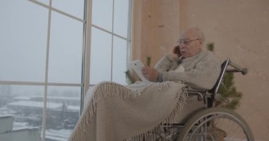 Evde tablet bilgisayar kullanan tekerlekli sandalyedeki yaşlı adam. Dokunma takımında fiziksel engelli internet tarayıcısı olan pozitif emekli erkek..