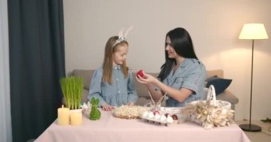 İyi tatiller. Anne ve kızı yumurta boyuyor. Aile Paskalya için hazırlanıyor. Sevimli küçük kız tavşan kulağı takıyor..