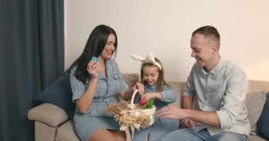 Avrupalı aile. Anne, baba ve kızı oturma odasında oturuyor. Komik kulaklı bir kız. Yumurtalarla sepeti paylaşmak.