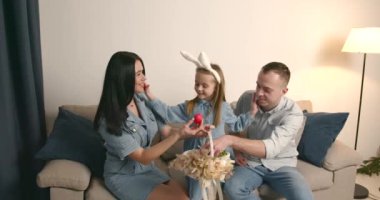 Avrupalı aile. Anne, baba ve kızı oturma odasında oturuyor. Komik kulaklı bir kız. Yumurtalarla sepeti paylaşmak.