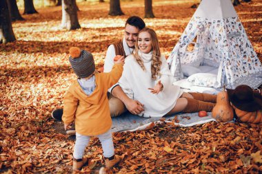 Aile sonbahar parkında eğlenir. Beyaz kazak içinde şirin bir hava kabarcığı. Küçük oğlu olan ebeveynler. Aile çadırın yanında oturuyor..