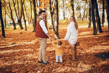 Aile sonbahar parkında eğlenir. Beyaz kazak içinde şirin bir hava kabarcığı. Küçük oğlu olan ebeveynler.
