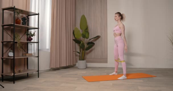 身材苗条的女人用电阻带做运动 身材苗条的女人用黄色的健身带做腿部运动 — 图库视频影像