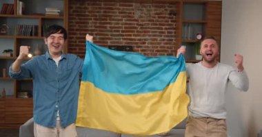 Mutlu futbol taraftarları Ukrayna spor takımına tezahürat yaparken kapalı alanda futbol şampiyonası izliyorlar. Ukrayna bayrağı taşıyan neşeli adamlar tezahürat yapıyorlar..