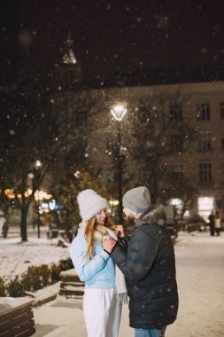Kış tatili gebeliği. Genç bir çiftin açık hava gece portresi. Avrupa sokaklarında poz vermek.