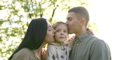 Parkta dururken küçük kızlarıyla kucaklaşan genç ebeveynler. Yaz sezonu. Kadın çocuk bekliyor..