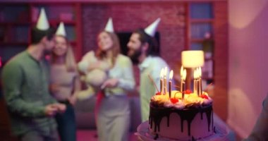 Parti şapkalı genç bir bayana mum üfleyen arkadaşlar. Evde gürültülü arkadaşlarla doğum gününü kutluyoruz..