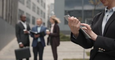Zarif görünümlü zarif bir kadın dışarıda duruyor ve tablet cihazıyla e-posta yolluyor. Güzel görünüşlü, gülümseyen iş kadını bilgisayarda tıklıyor ve kayıyor. İş konsepti.