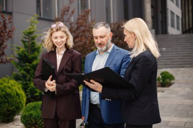 Modern ofis binasının önünde kendinden emin iş adamları konuşuyor. Kadın ve erkek belgelere bakıyor. Bankacılık ve finans piyasası kavramı.