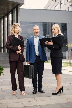 Modern ofis binasının önünde kendinden emin iş adamları konuşuyor. Kadın ve erkek belgelere bakıyor. Bankacılık ve finans piyasası kavramı.