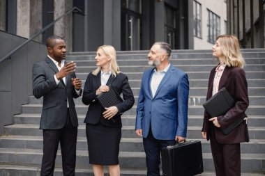 Modern ofis binasının önünde duran kendinden emin iş adamları. Erkekler ve kadınlar ellerinde belgelerle konuşuyor. Bankacılık ve finans piyasası kavramı.