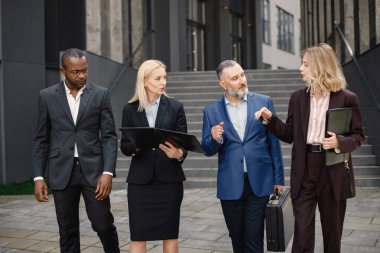 Modern ofis binasının önünde duran kendinden emin iş adamları. Erkekler ve kadınlar ellerinde belgelerle konuşuyor. Bankacılık ve finans piyasası kavramı.