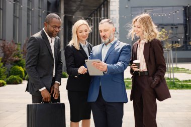 Modern ofis binasının önünde duran kendinden emin iş adamları. Erkekler ve kadınlar konuşuyorlar ve belgelere bakıyorlar. Bankacılık ve finans piyasası kavramı.