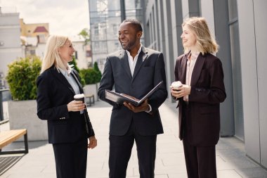 Modern ofis binasının önünde duran kendinden emin iş adamları. Siyahi adam ve beyaz kadın konuşuyorlar ve belgelere bakıyorlar. Bankacılık ve finans piyasası kavramı.