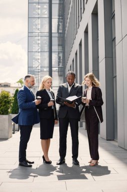 Modern ofis binasının önünde duran kendinden emin iş adamları. Erkekler ve kadınlar konuşuyorlar ve belgelere bakıyorlar. Bankacılık ve finans piyasası kavramı.