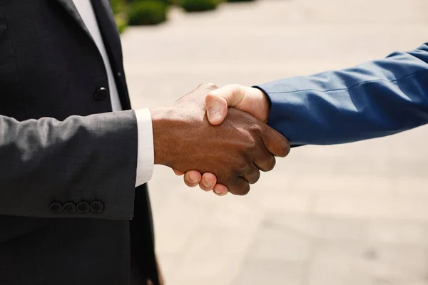 Close up of hands of black and caucasian business men shaking hands outdoors. Building a network towards success.