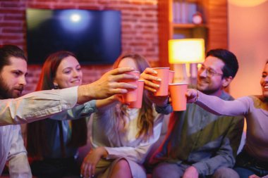 İçeceklerle dolu bir kağıt kutunun kesilmiş fotoğrafı. Akşamki kırmızı ışıkta otobüste oturan beş arkadaş. İki erkek ve üç kız kağıt bardakla içki tokuşturuyorlar..