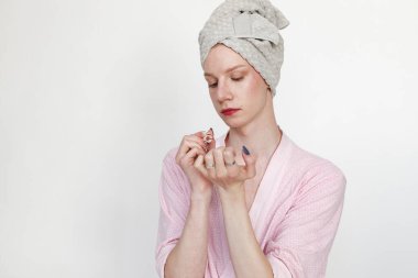 Makyajlı genç bir adam manikür yapıyor. Pembe sabahlık giyen ve kafasında havlu olan bir adam. Beyaz arkaplanda izole edilmiş adam.