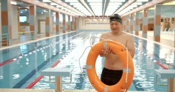 アジア人男性プールで生命リングを保持する スイミングプールの近くの男性水泳 — ストック動画
