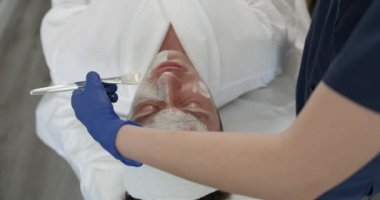 Kozmetik uzmanı spa salonundaki erkeklerin yüzüne kilden maske takıyor. Güzellik uzmanı, güzellik salonunda yakışıklı bir adam için tedavi görüyor..