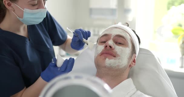 顔の皮膚を調べる有資格の美容師ながら 男性のクライアントは鏡を見て 医療美容室での手続き — ストック動画