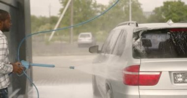 Young man washing his car at a manual car wash. Black man washing his car with foam at at self service outdoors. Clean concept. Car washing concept.