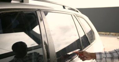 Car detailing. Black man wiping water from car window with squeegee rubber by hand.