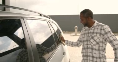 Car wash and cleaning at outdoors self service station. Shot of handsome young black guy silver car with a yellow microfiber cloth outdoors.