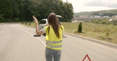 Upset young woman driver talking angrily on cell phone with assistance service near a broken car. Accident on the road concept.