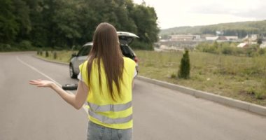 Upset young woman driver talking angrily on cell phone with assistance service near a broken car. Accident on the road concept.