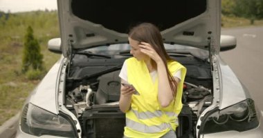 Upset young woman driver talking angrily on cell phone with assistance service near a broken car. Accident on the road concept.