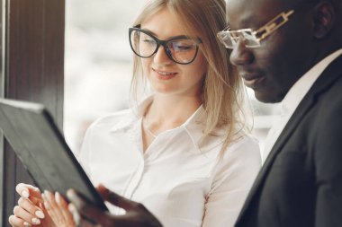 African man. Guy in a black suit. Students with a talet. Girl in white blouse. International people in a cafe.