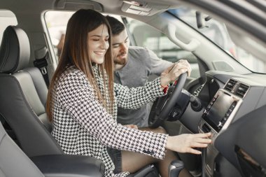 Young and cheerful woman enjoying new car while sitting inside. Man helping her to understand evetything. Girl wearing black costume.