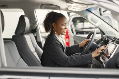 Young and cheerful woman enjoying new car while sitting inside. Black woman driving a car. Girl wearing black costume.