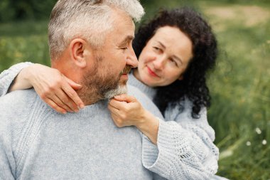 Close up romantic couple sitting in autumn park and hugging in daytime. Man and woman wearing blue sweaters. Focus on a womans face.