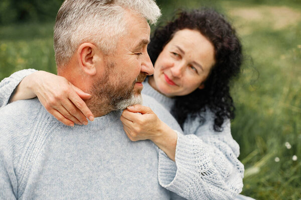 Close up romantic couple sitting in autumn park and hugging in daytime. Man and woman wearing blue sweaters. Focus on a womans face.