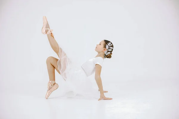 Little ballerina on white background. Brunette girl wearing white ballet suit. Girl sitting on a floor.